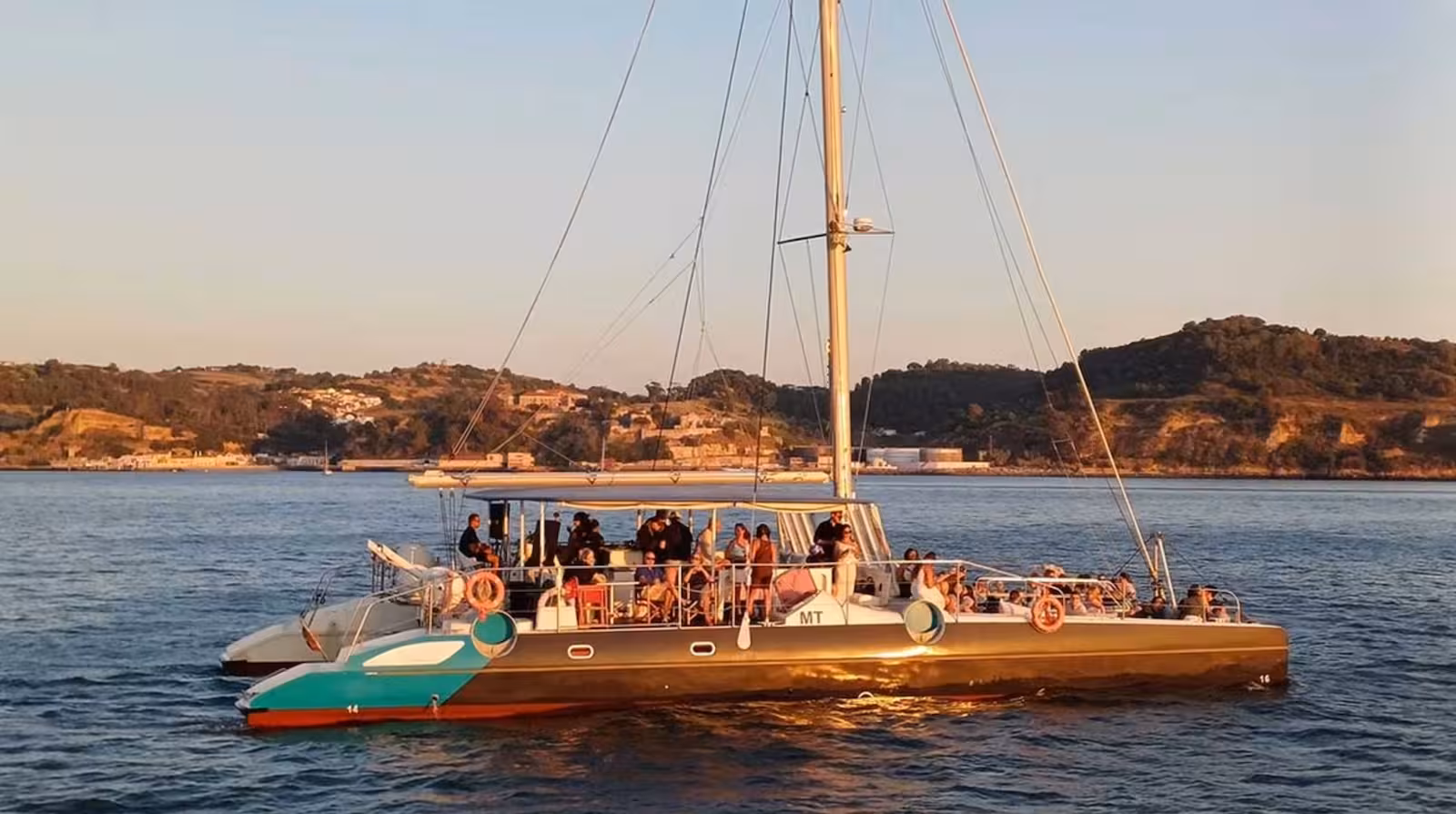 Luz del atardecer ilumina el catamarán Tartaruga con las velas desplegadas en el río Tajo, Lisboa.